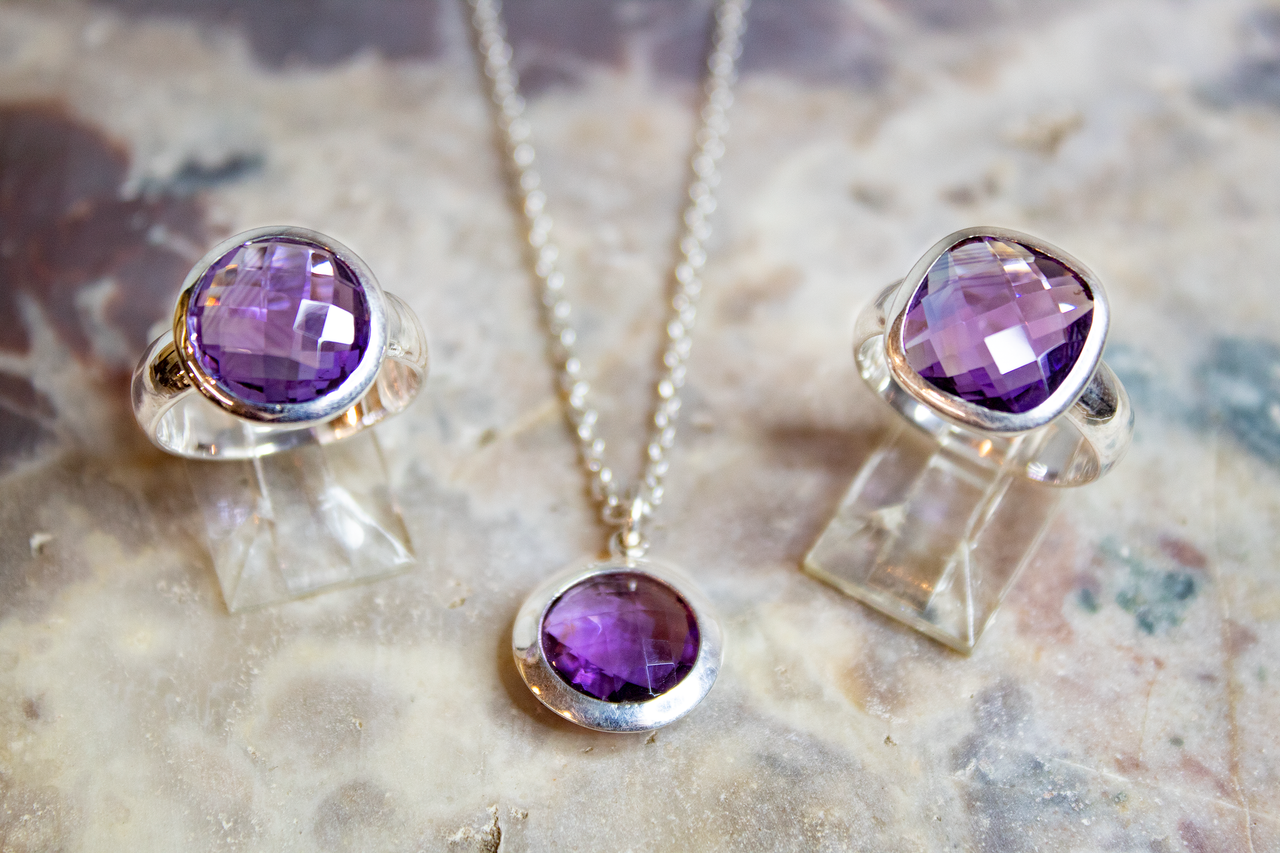 Men's Jewelry Close-up of amethyst rings and necklace set on a textured surface, showcasing silver accents.