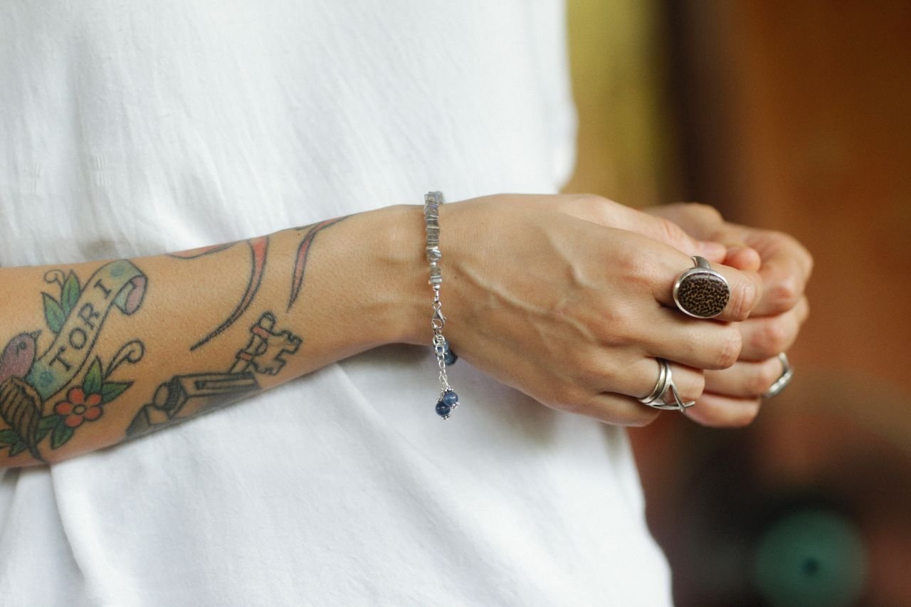 Personalized Jewelry Close-up of a tattooed arm adorned with bracelets and rings, showcasing personal style.