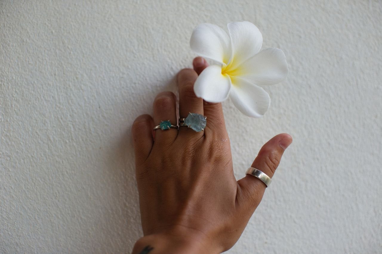 Stacking Rings Close-up of a hand adorned with rings holding a delicate white flower against a textured wall.