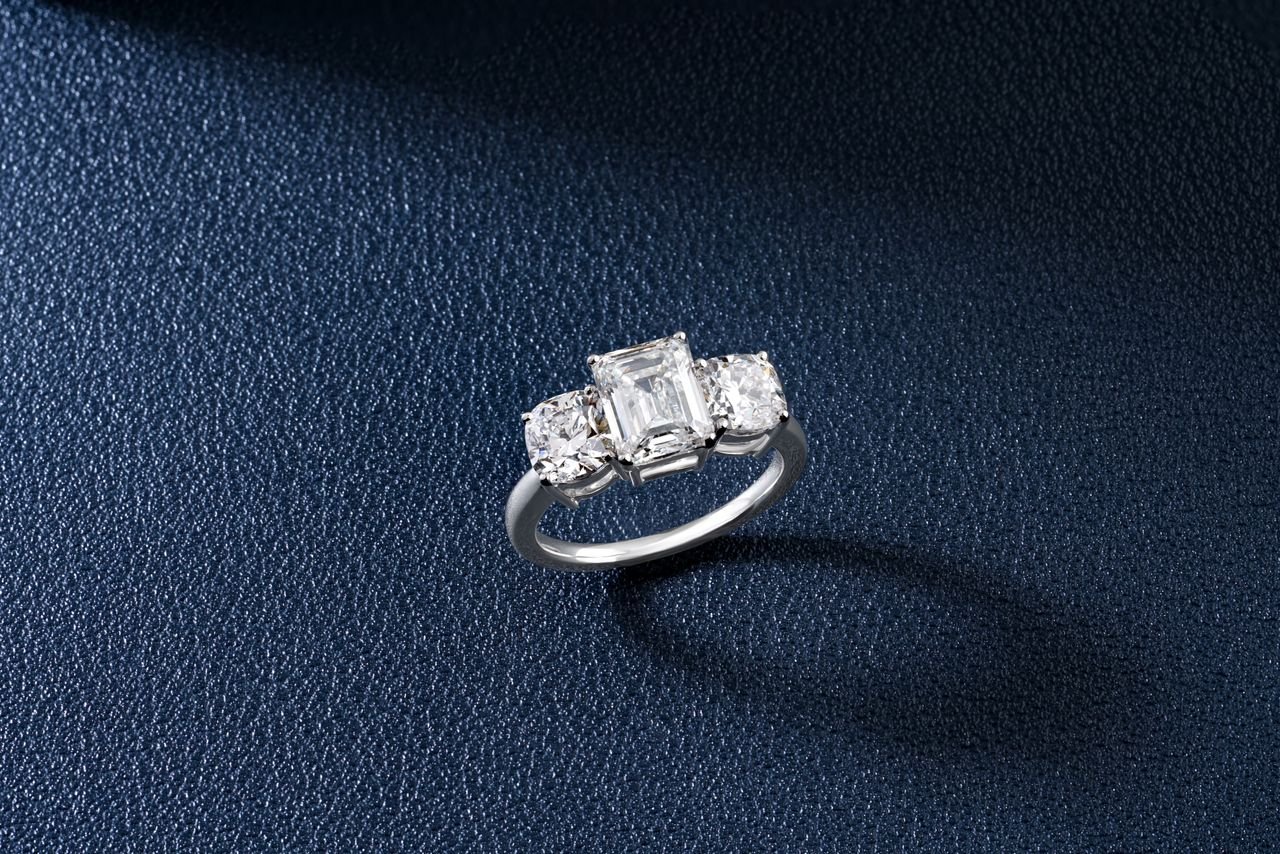 Sophisticated close-up of a sparkling three-stone diamond ring on a textured blue surface.