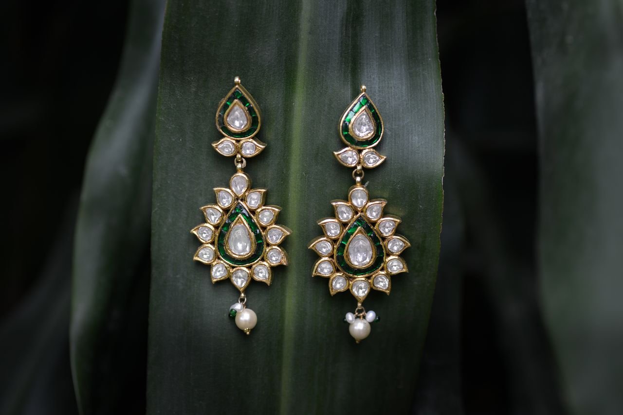 Sophisticated gold and pearl earrings displayed against lush green foliage.