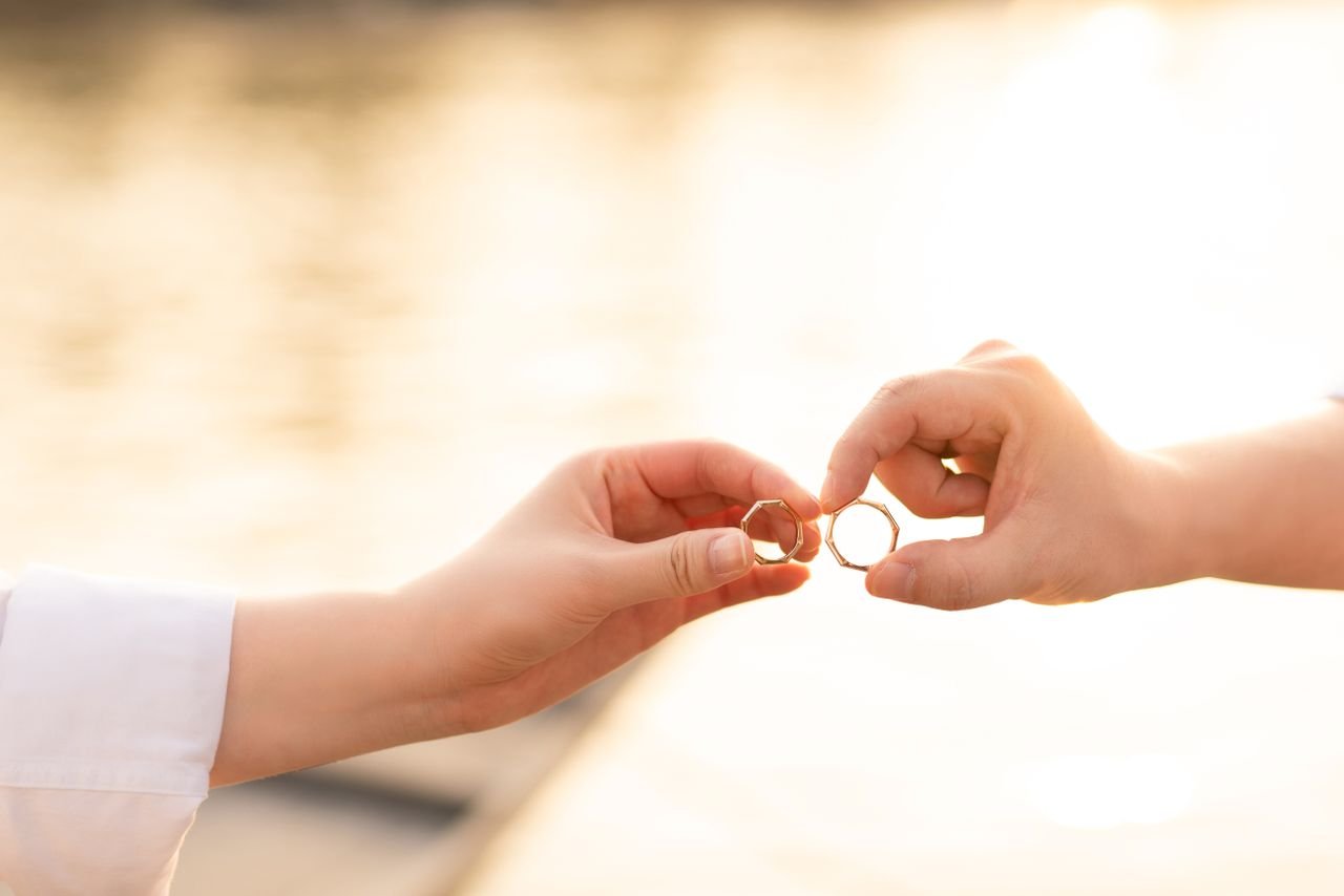 Promise Rings A close-up of two hands exchanging wedding rings against a sunset background, symbolizing unity.