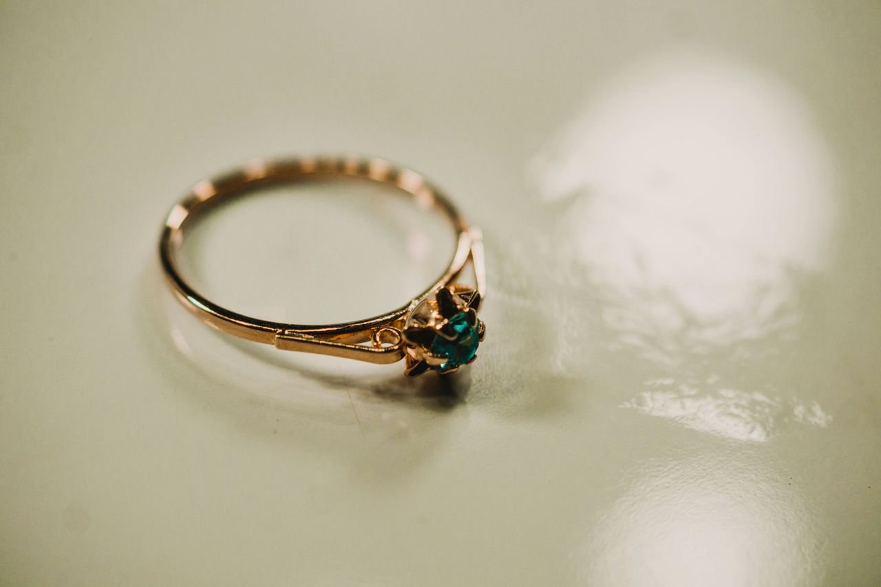 Cocktail Rings Close-up of a delicate gold ring with a green gemstone reflecting light on a smooth surface.