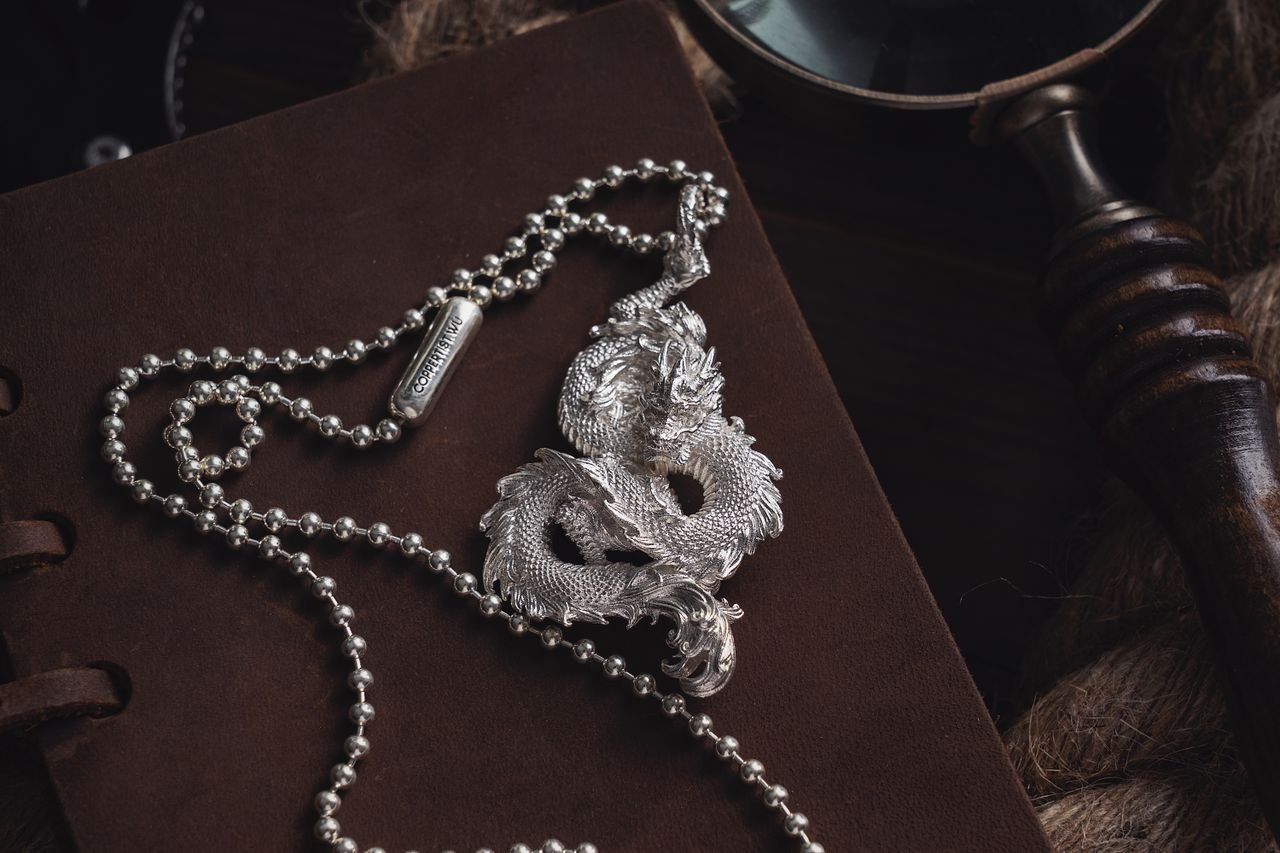 Elegant silver dragon pendant necklace on a dark leather surface showcasing detailed craftsmanship.