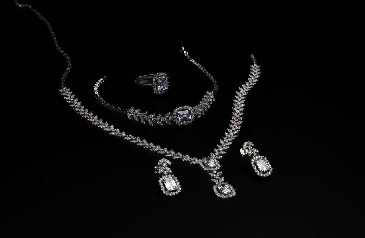 Tennis Necklaces Elegant diamond jewelry set including necklace, bracelet, ring, and earrings on a black backdrop.
