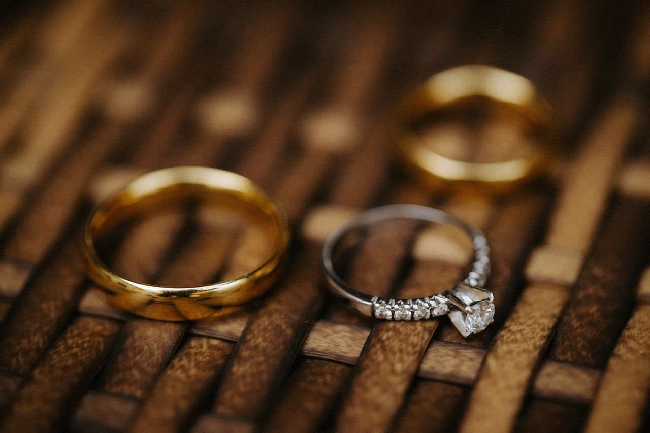 Close-up of wedding and engagement rings on woven surface, highlighting gold and diamonds.