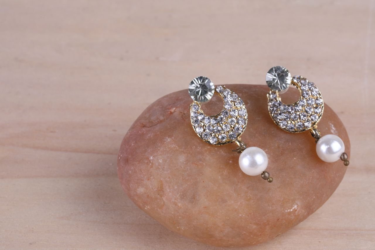 Sparkling diamond and pearl earrings elegantly displayed on a stone for a stylish look.