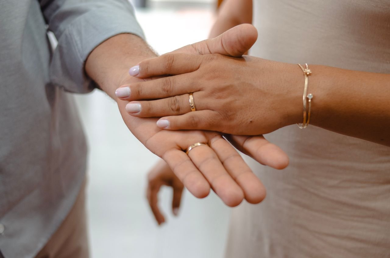 Personalized Jewelry Close-up of a couple holding hands showcasing gold rings and bracelets.