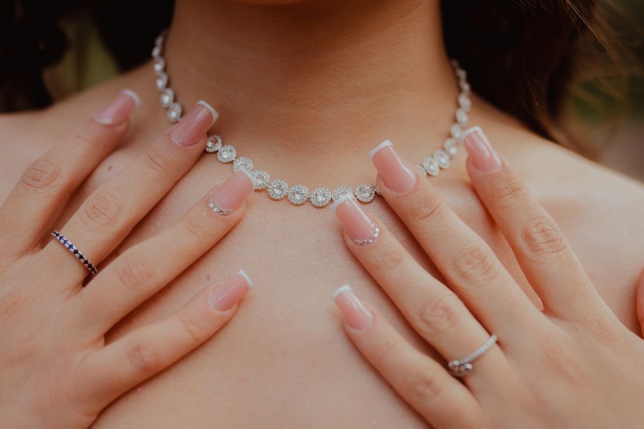 Tennis Necklaces Close-up of elegant diamond necklace and manicured hands, showcasing jewelry fashion and style.