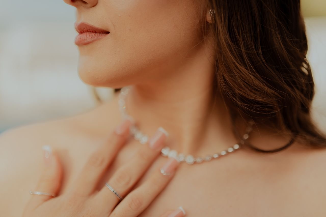 Tennis Necklaces Close-up of a woman touching her diamond necklace with manicured nails.