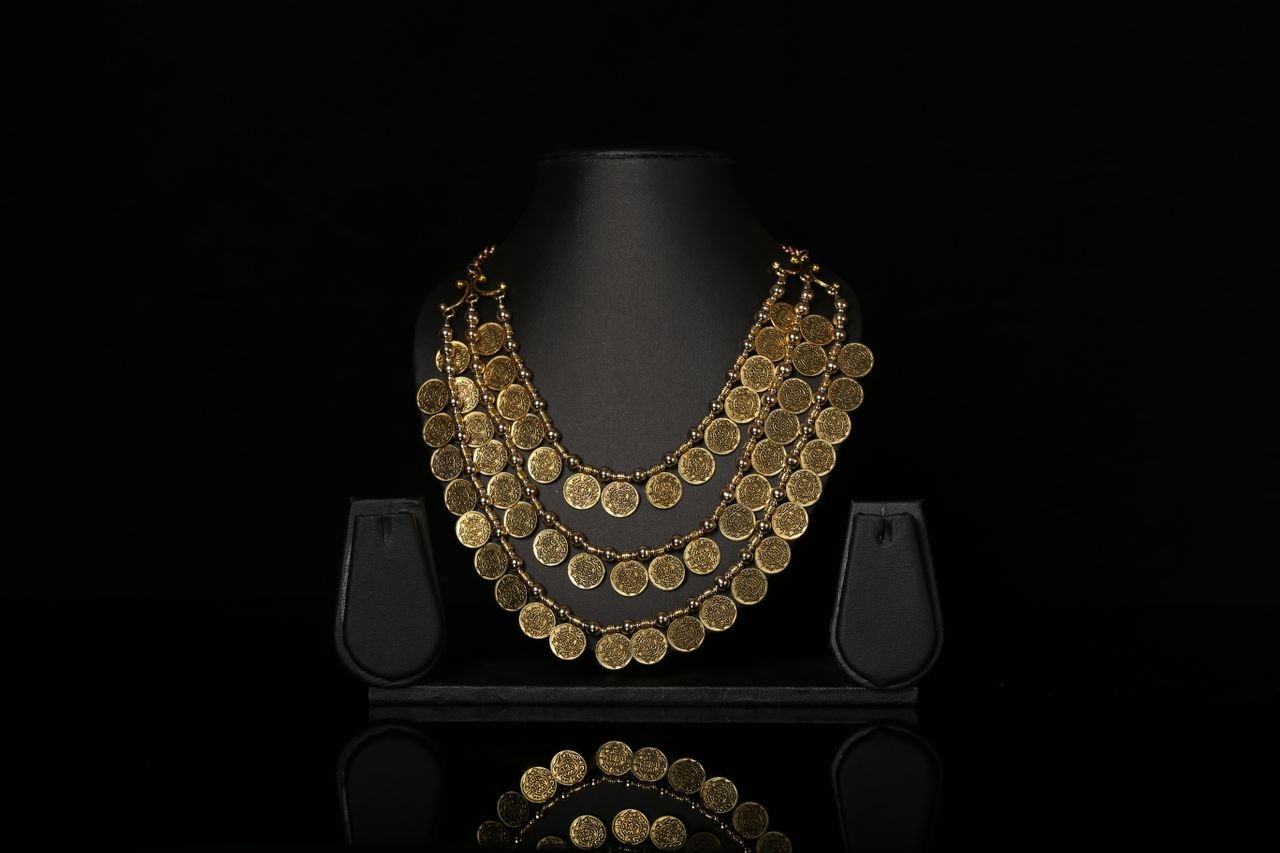Necklaces Luxurious gold coin necklace elegantly displayed on a black stand against a dark background.