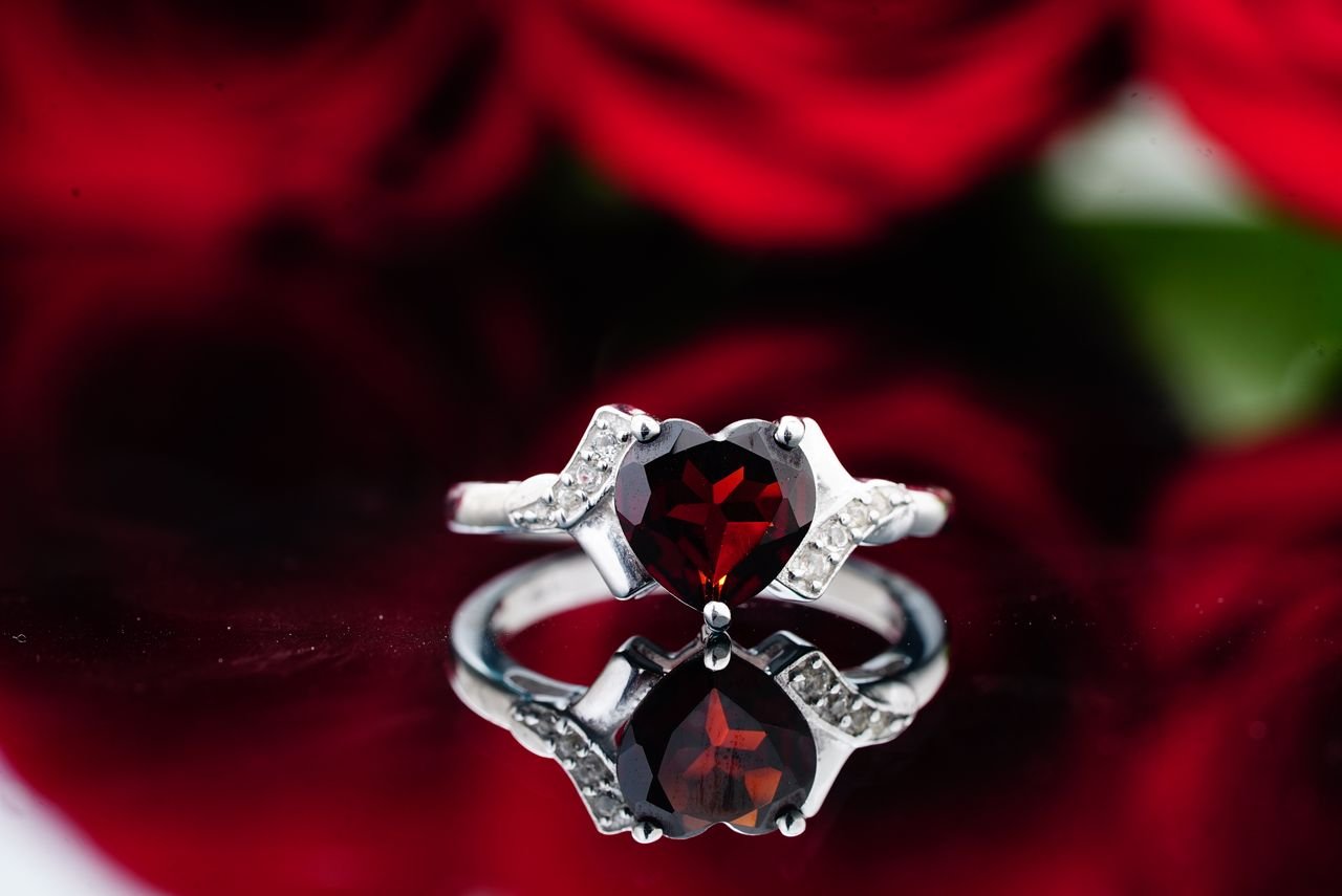 Cocktail Rings Ring with small crystals and red ruby stone placed on reflective surface against red roses
