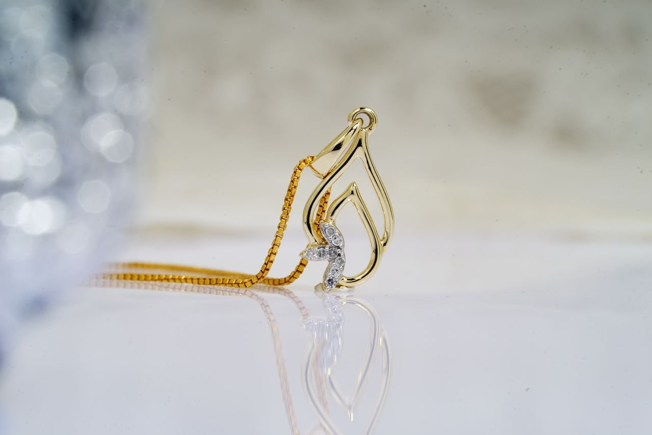 Personalized Jewelry Small precious diamonds in golden shiny pendant on necklace placed on reflective white surface of table