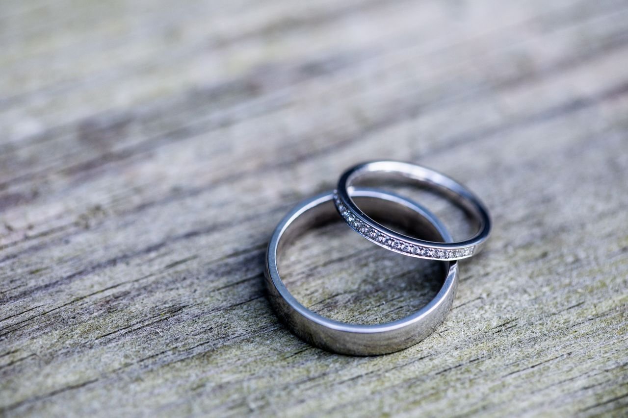 Promise Rings Close-up of elegant silver wedding bands, one set with diamonds, on a rustic wooden surface.