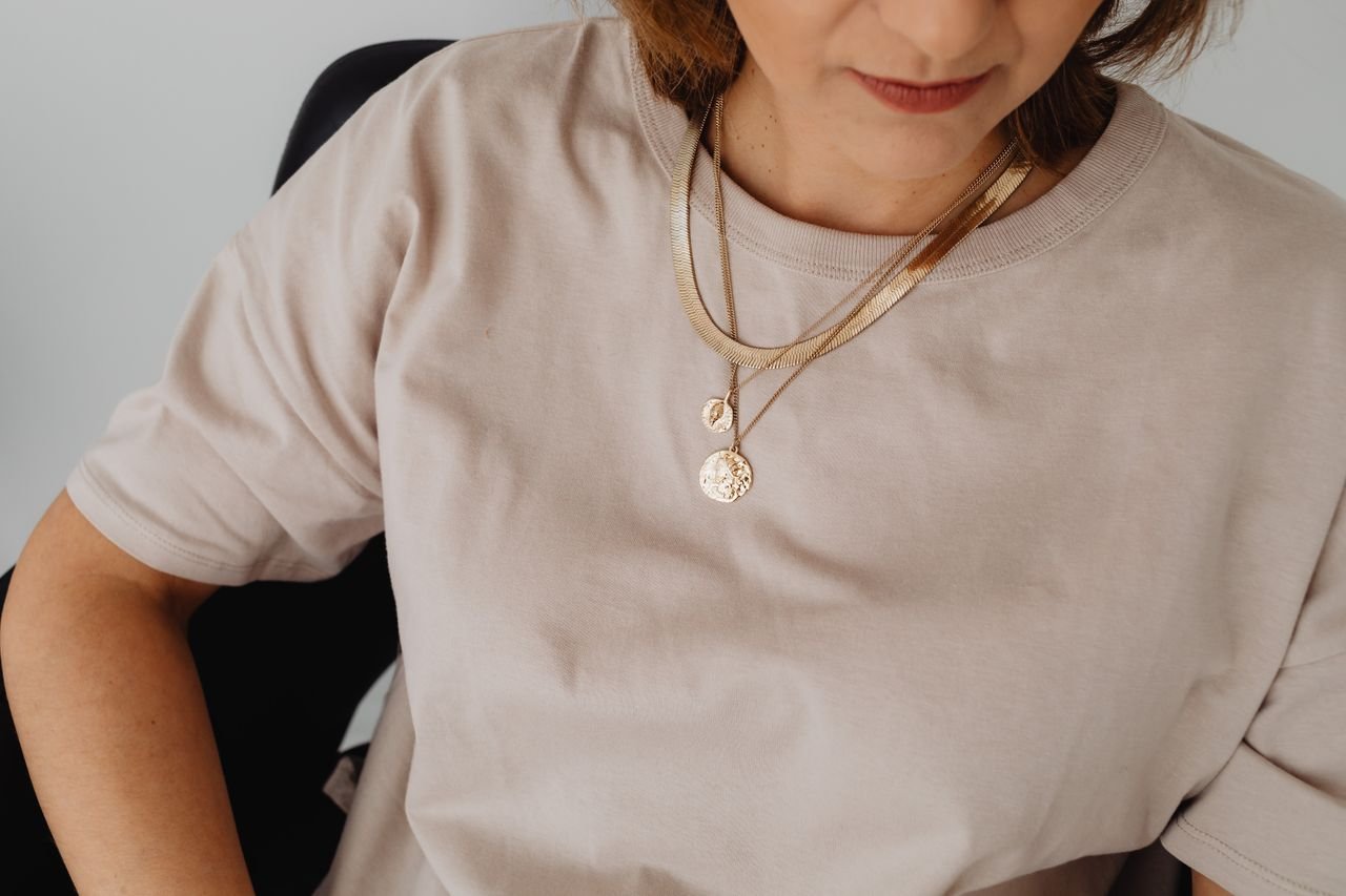 Tennis Necklaces Close-up of a woman wearing a beige shirt with a layered gold necklace.