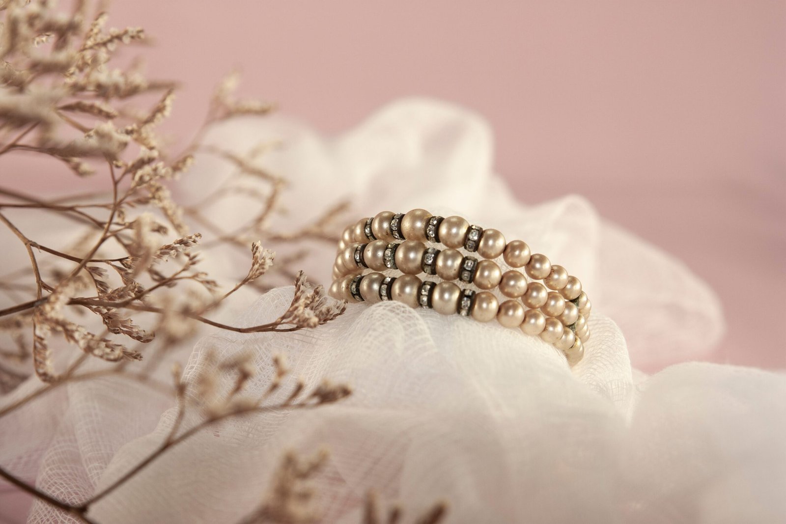 Close-up of a pearl bracelet with delicate details on a soft pink fabric.