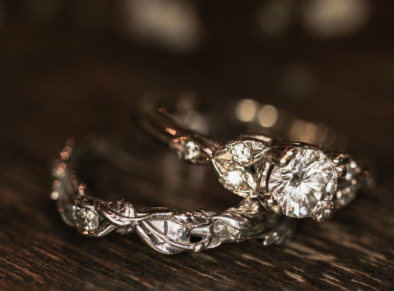 Close-up of elegant silver engagement and wedding rings with diamonds on a wooden surface.